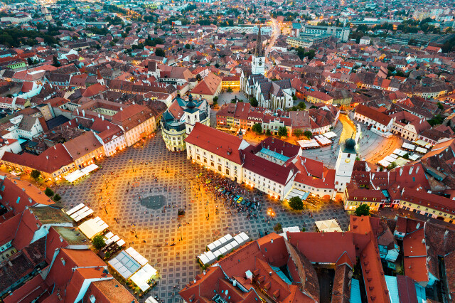 Aerial drone view of the Historic Centre of Sibiu at evening, Romania. The Great Square with Sibiu Lutheran Cathedral and old buildings around, narrow streets, people, illumination