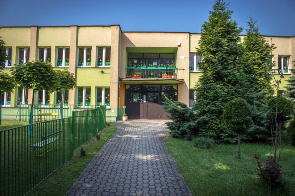 Piętrowy budynek o żółto-zielonej elewacji z&nbsp;chodnikiem prowadzącym do&nbsp;wejścia, otoczony drzewami i&nbsp;zielonym ogrodzeniem.