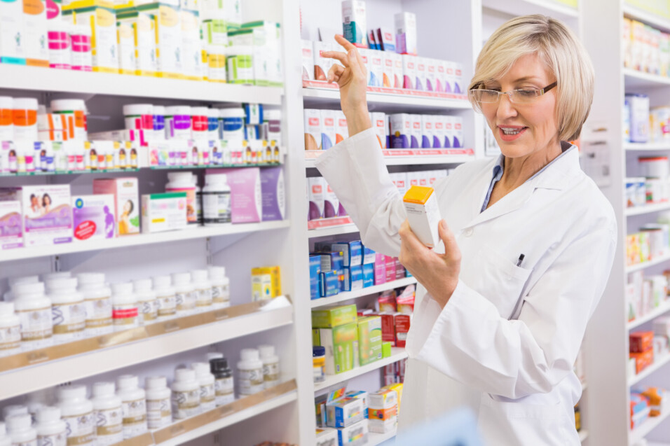 Smiling pharmacist looking at medicine in the pharmacy - Smiling pharmacist looking at medicine in the pharmacy